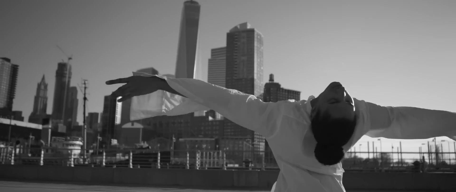 Une silhouette en chemise blanche se penche en arrière devant la skyline de Lower Manhattan.
